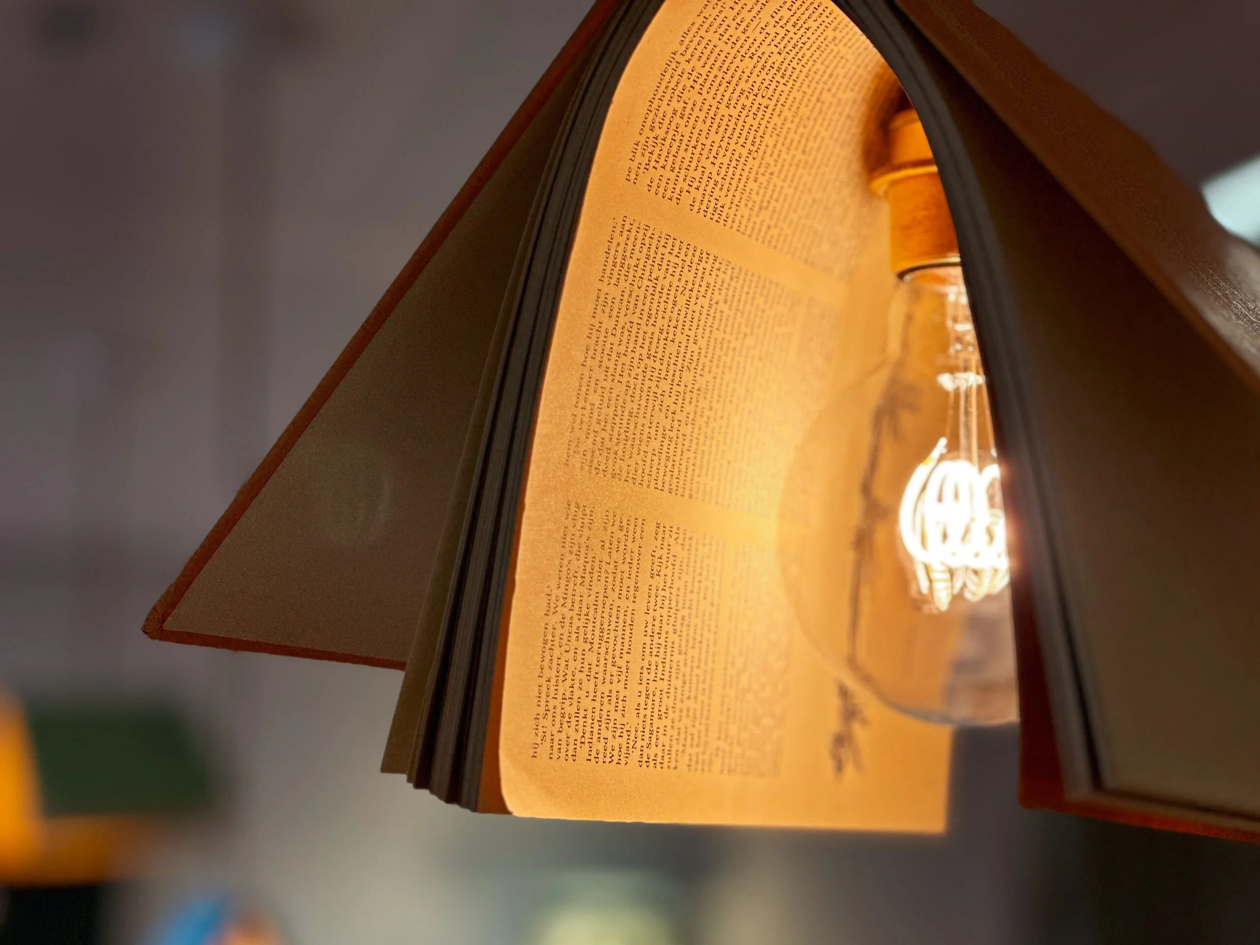 A book repurposed as a lampshade with an exposed vintage light bulb glowing warmly.