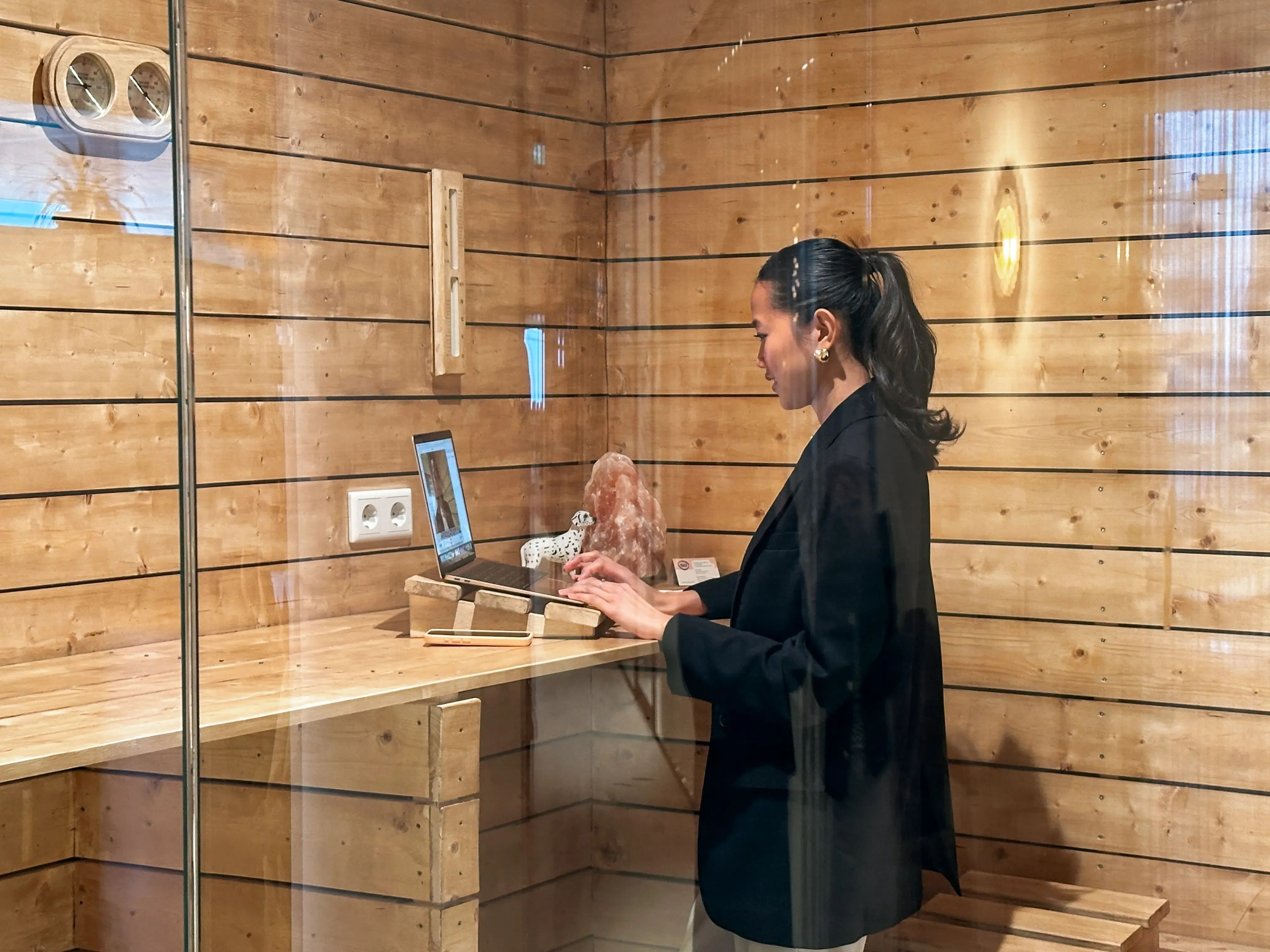 Vrouw die op een laptop werkt in belhokje in houten sauna stijl