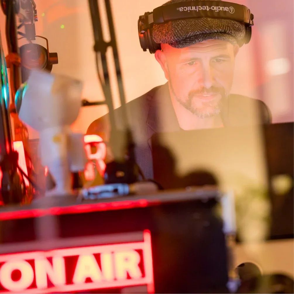 Man met koptelefoon en pet in een studio met een bordje ‘ON AIR’.