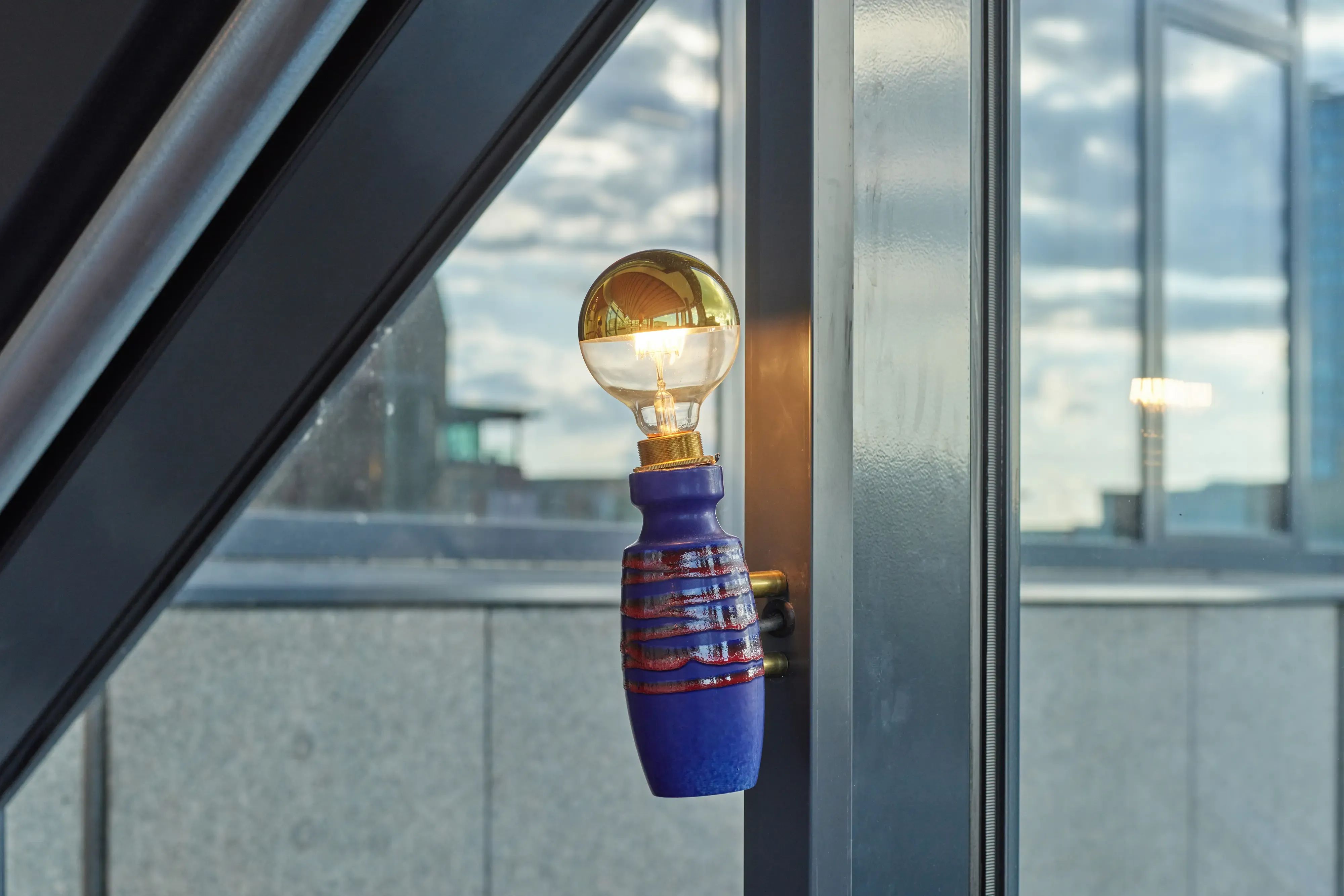 Een unieke blauw-gouden lamp met een geribbelde voet verlicht een moderne binnenruimte.