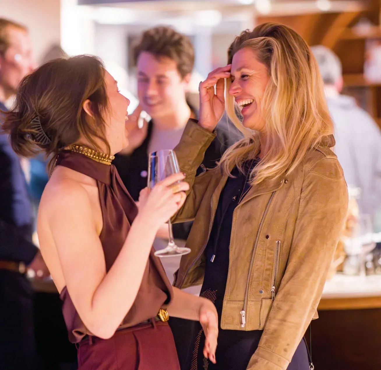 Twee vrouwen lachen en praten vrolijk tijdens een sociale bijeenkomst, met een drankje in hun hand.