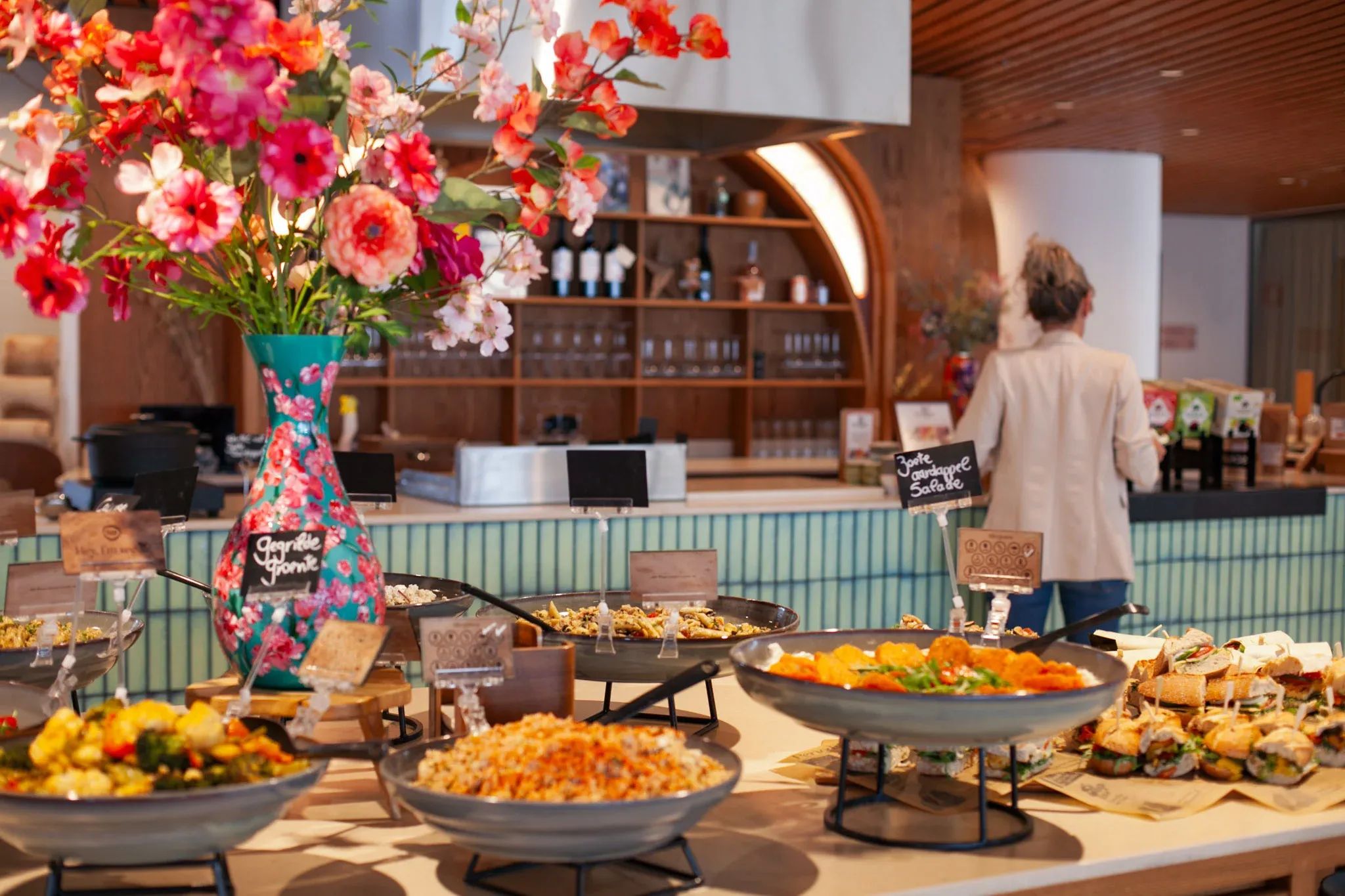 Vibrant buffet table displaying diverse dishes and colorful flowers, with a person serving.