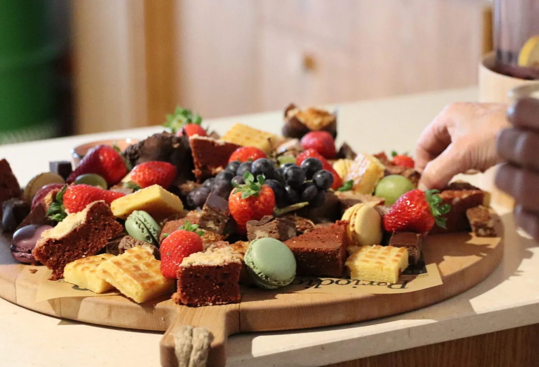 Assortiment brownies, minicakes, kleurrijke macarons, aardbeien en bosbessen op een houten plank.