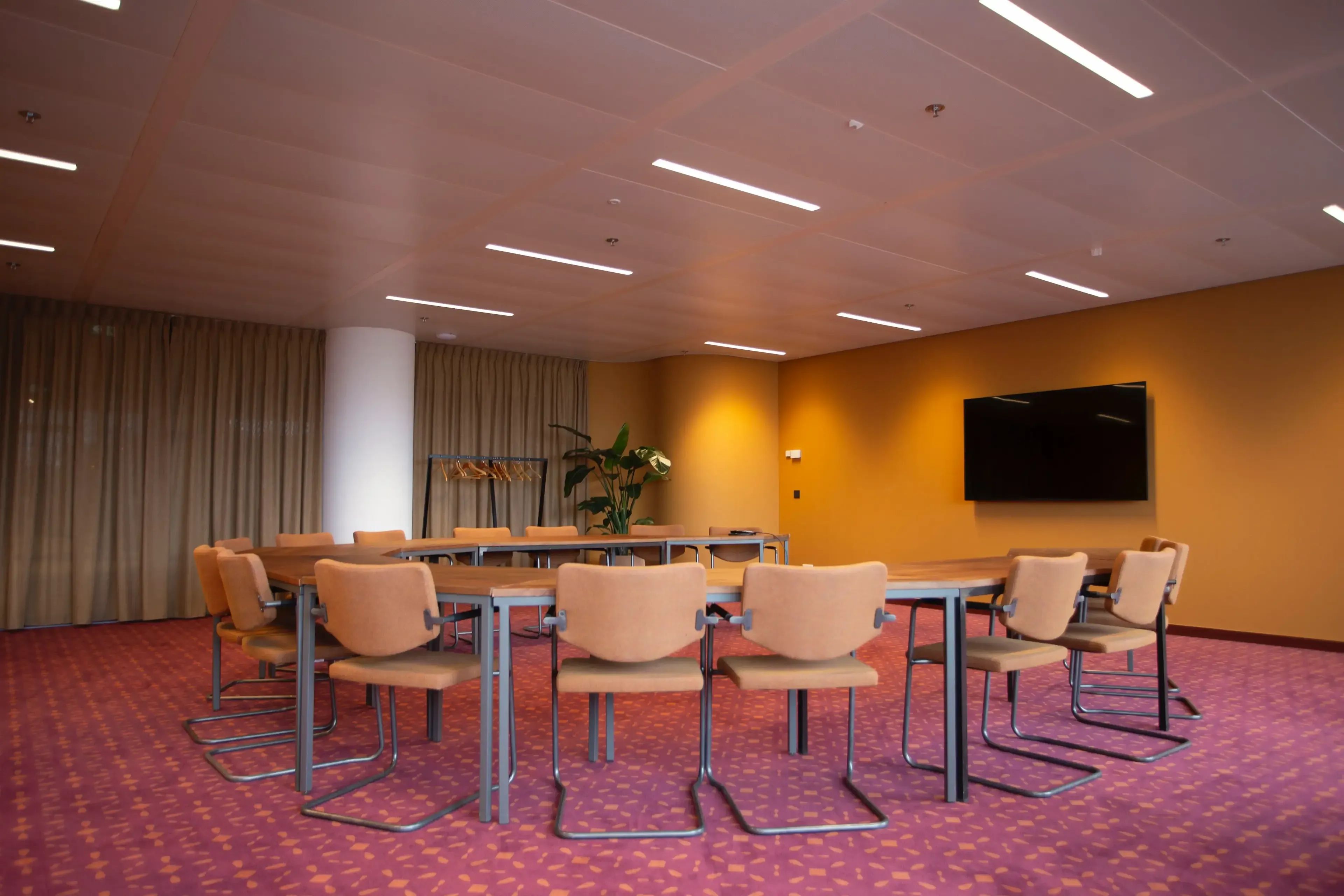 Moderne vergaderruimte met een grote ovale tafel, stoelen, flatscreen-tv en rode loper.