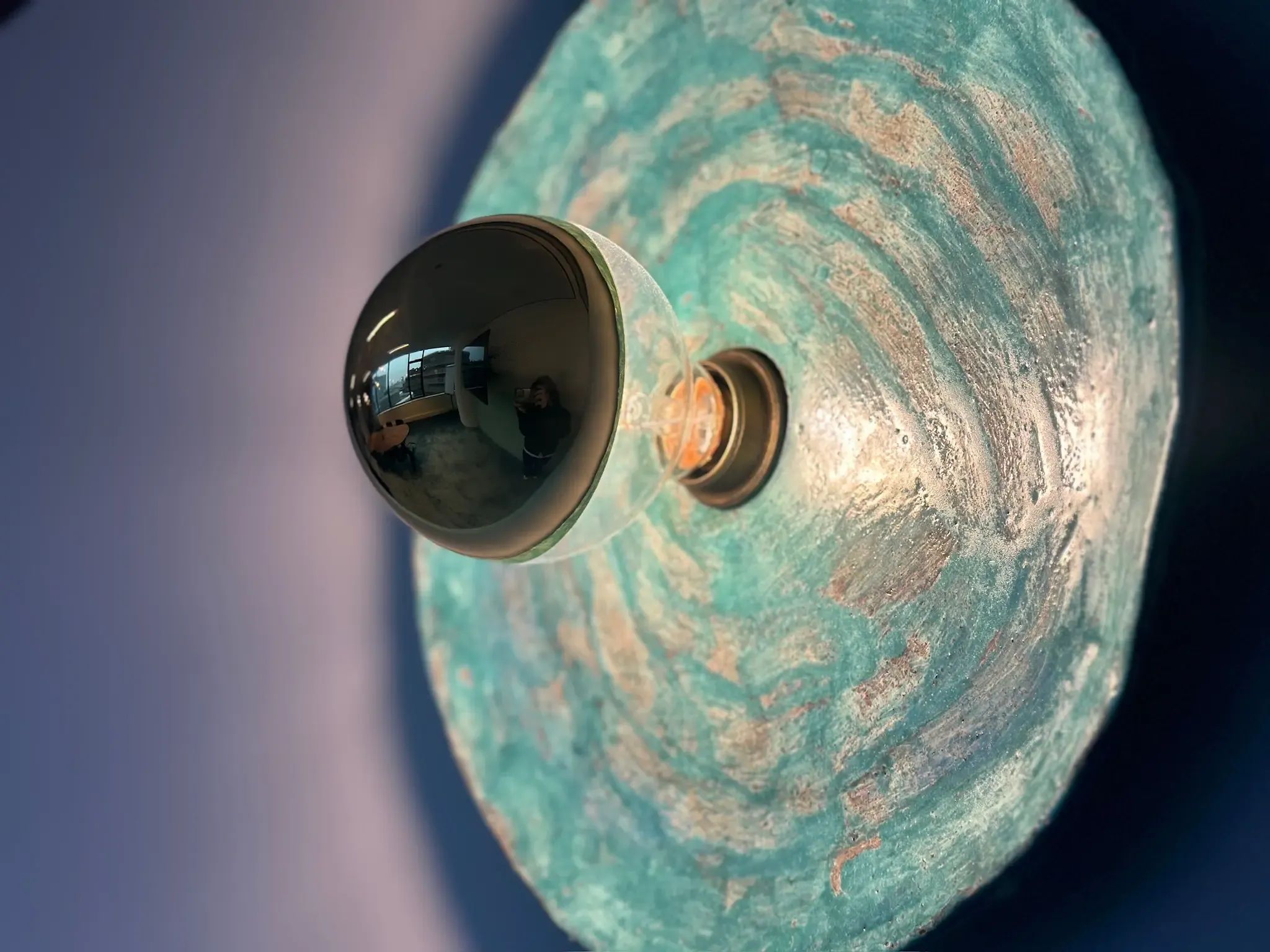Een unieke wandlamp met een gestructureerde blauwgroene organische achterplaat en een bolvormige lamp.