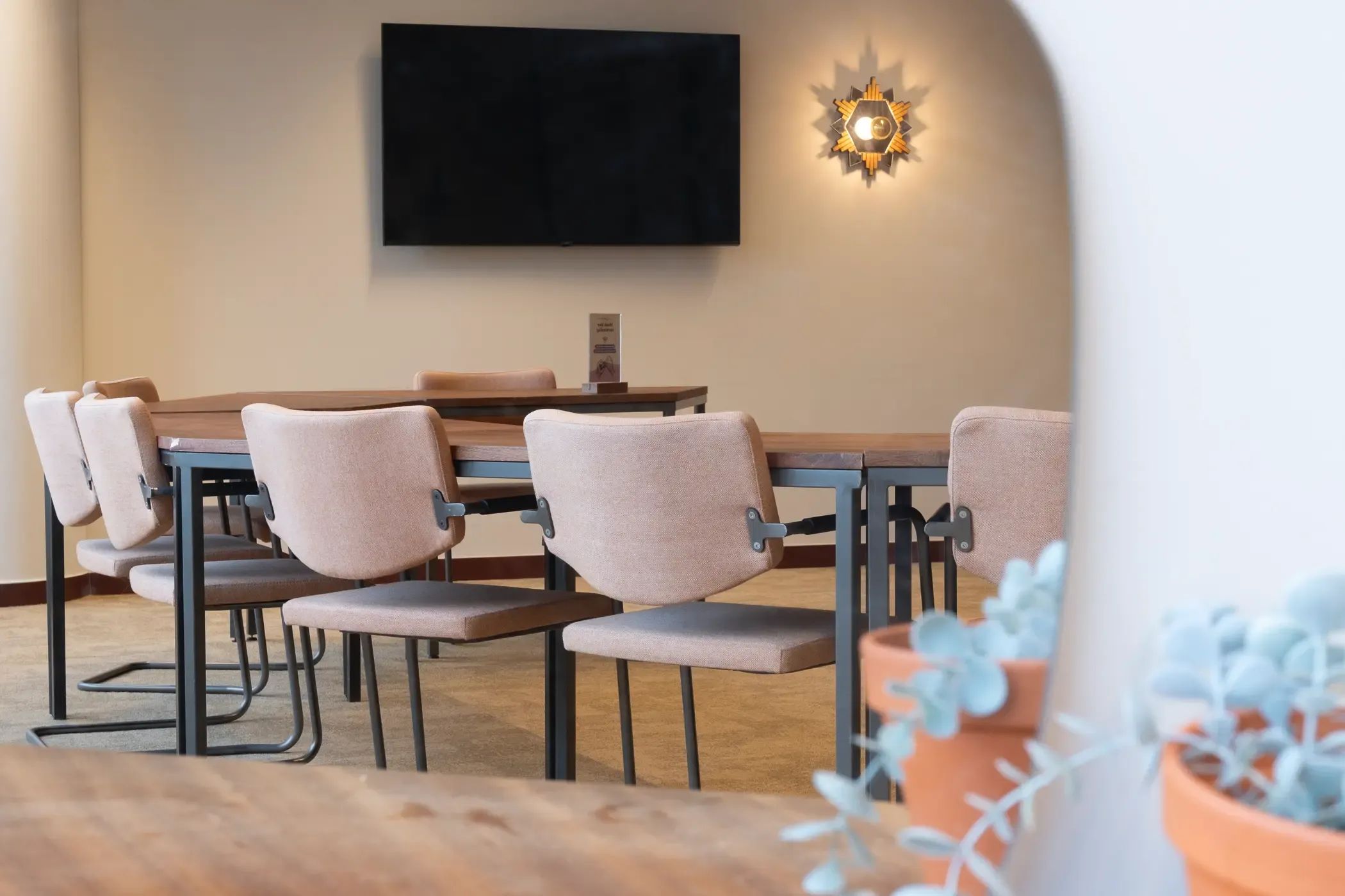 Moderne vergaderruimte met een houten tafel, stoelen, een aan de muur bevestigde tv en decoratieve verlichting.
