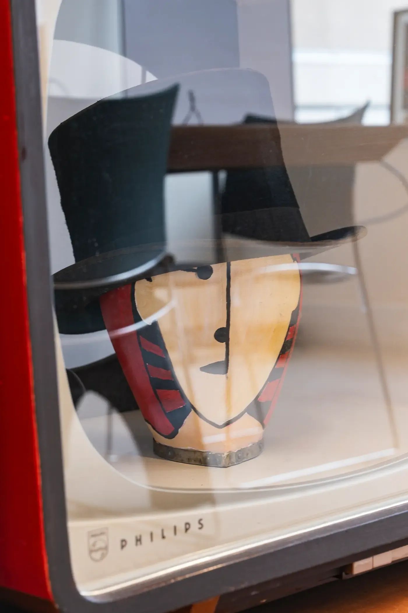 Een zwarte hoge hoed, een masker en een hoed tentoongesteld in een vitrine.