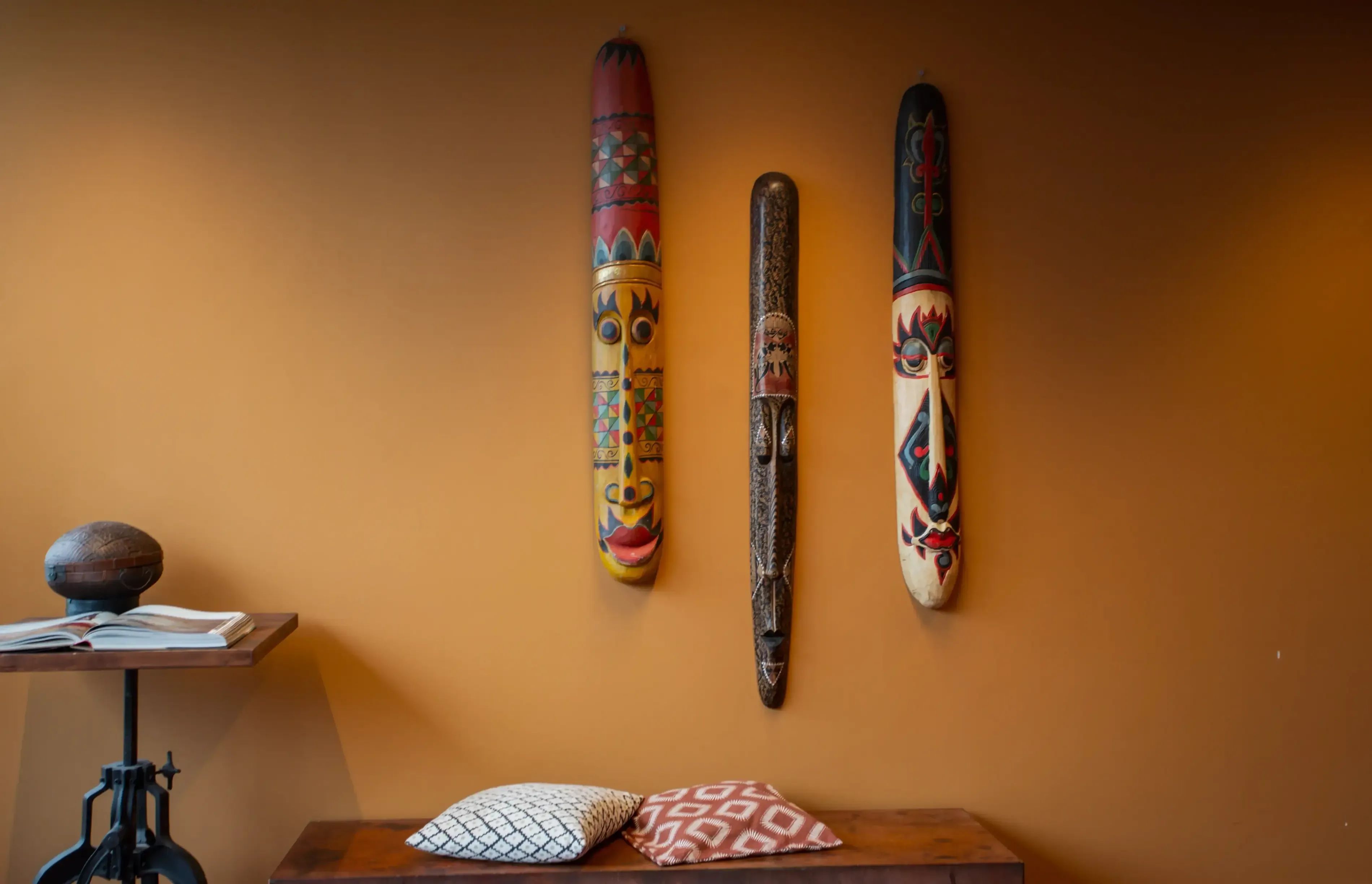 Drie fijn bewerkte decoratieve voorwerpen hangen verticaal aan een warme oranjebruine muur.