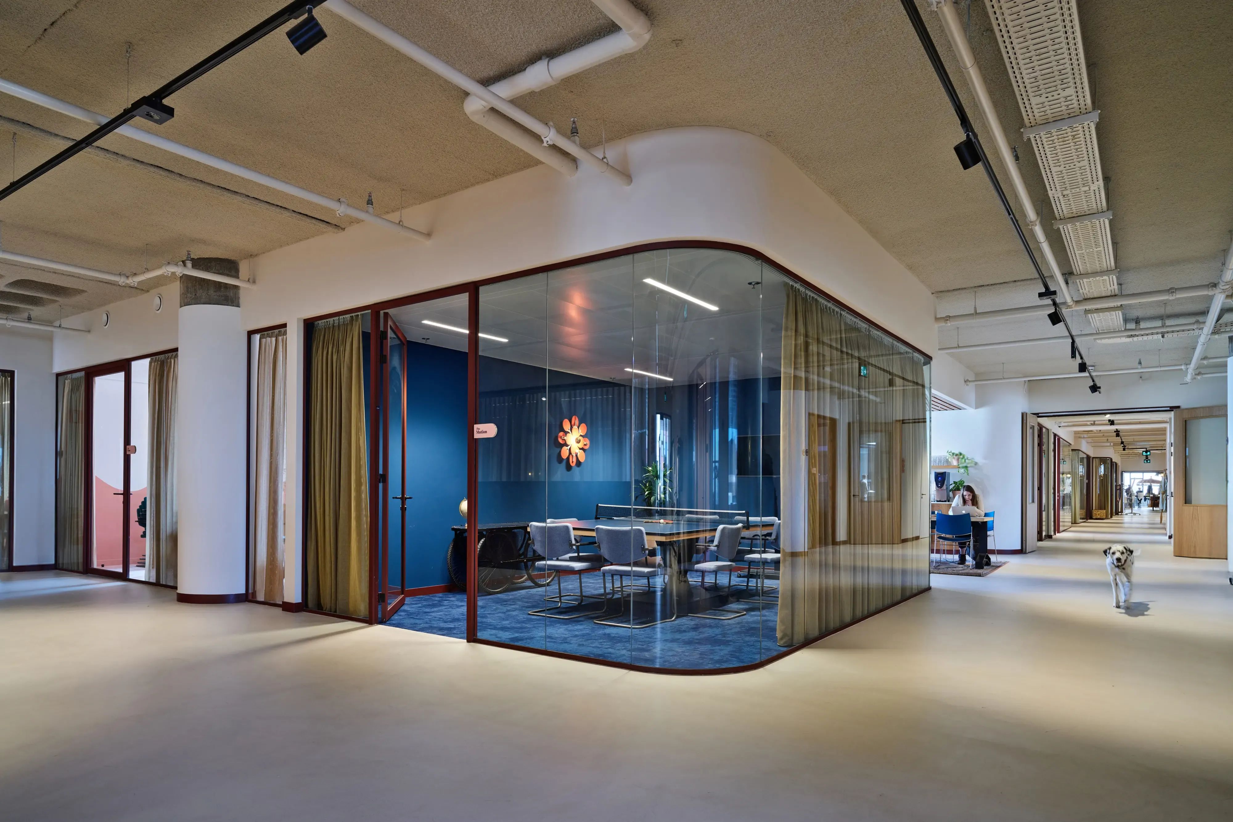 Modern kantoor met een vergaderruimte met gebogen glas, blauwe muur en ronde vergadertafel.