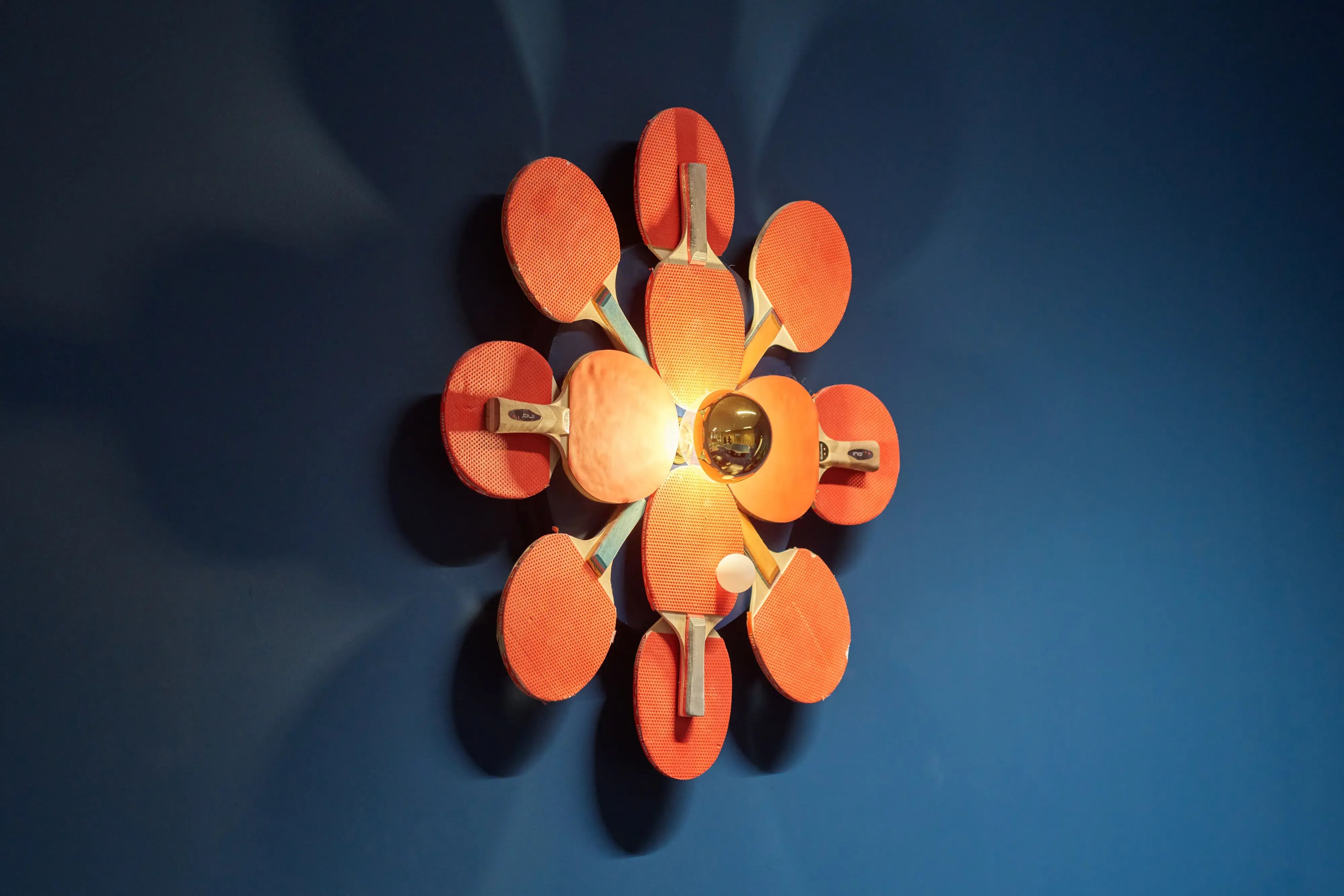 Een unieke wandlamp gemaakt van oranje pingpongbatjes die rond een centrale lamp zijn gerangschikt.