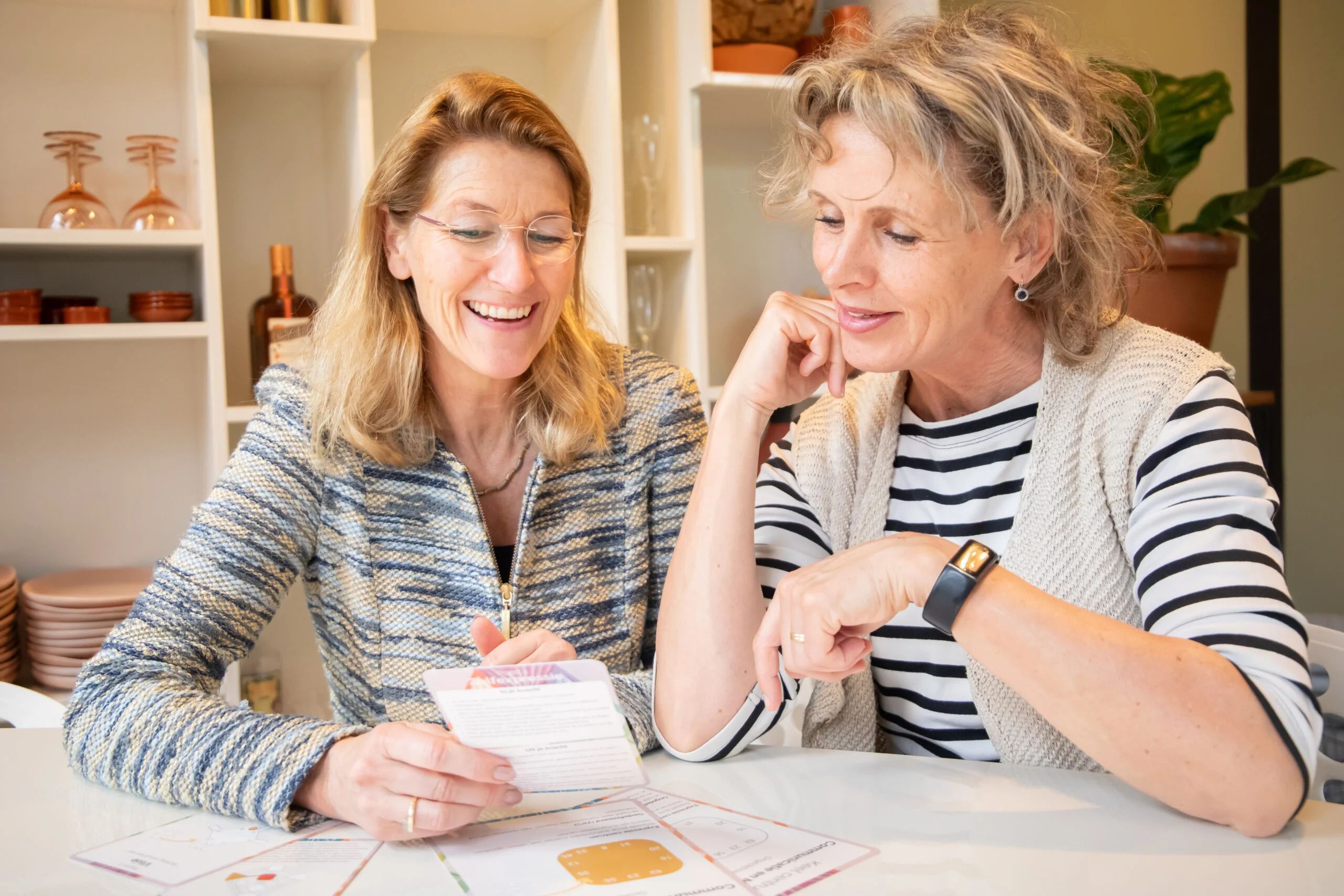 Two smiling women attentively examine documents together at a bright table indoors.