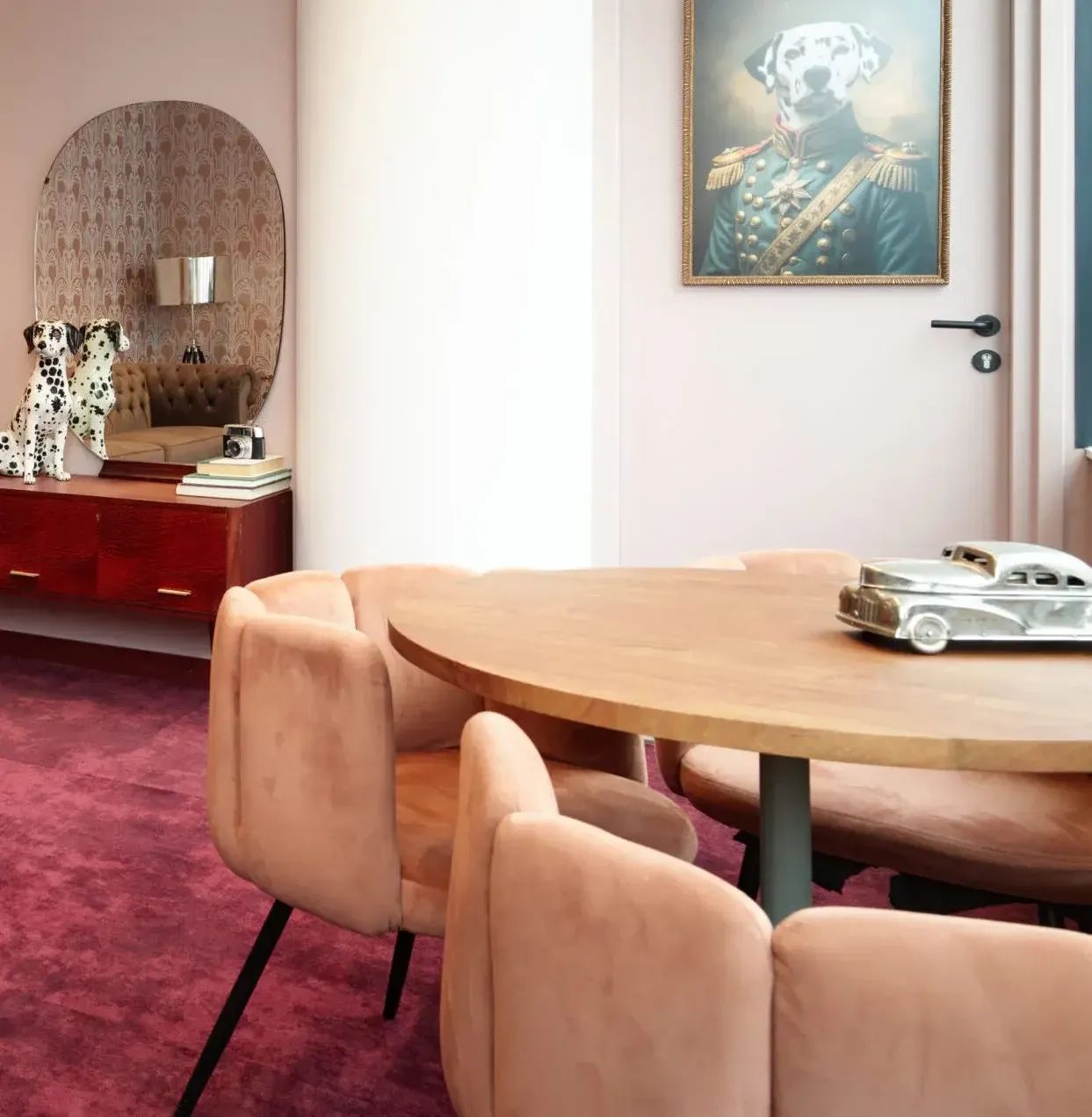 Moderne eetkamer met roze fluwelen stoelen, ronde tafel en kunstwerk met hondenportret.
