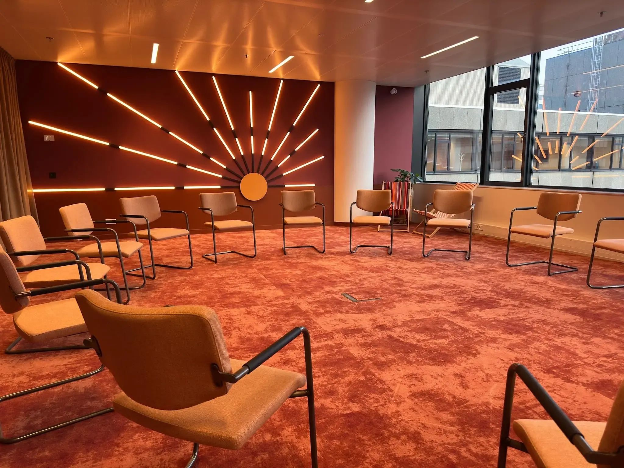 Moderne vergaderruimte: stoelen in een cirkel op rood tapijt, wanddecoratie met zonnestralen.