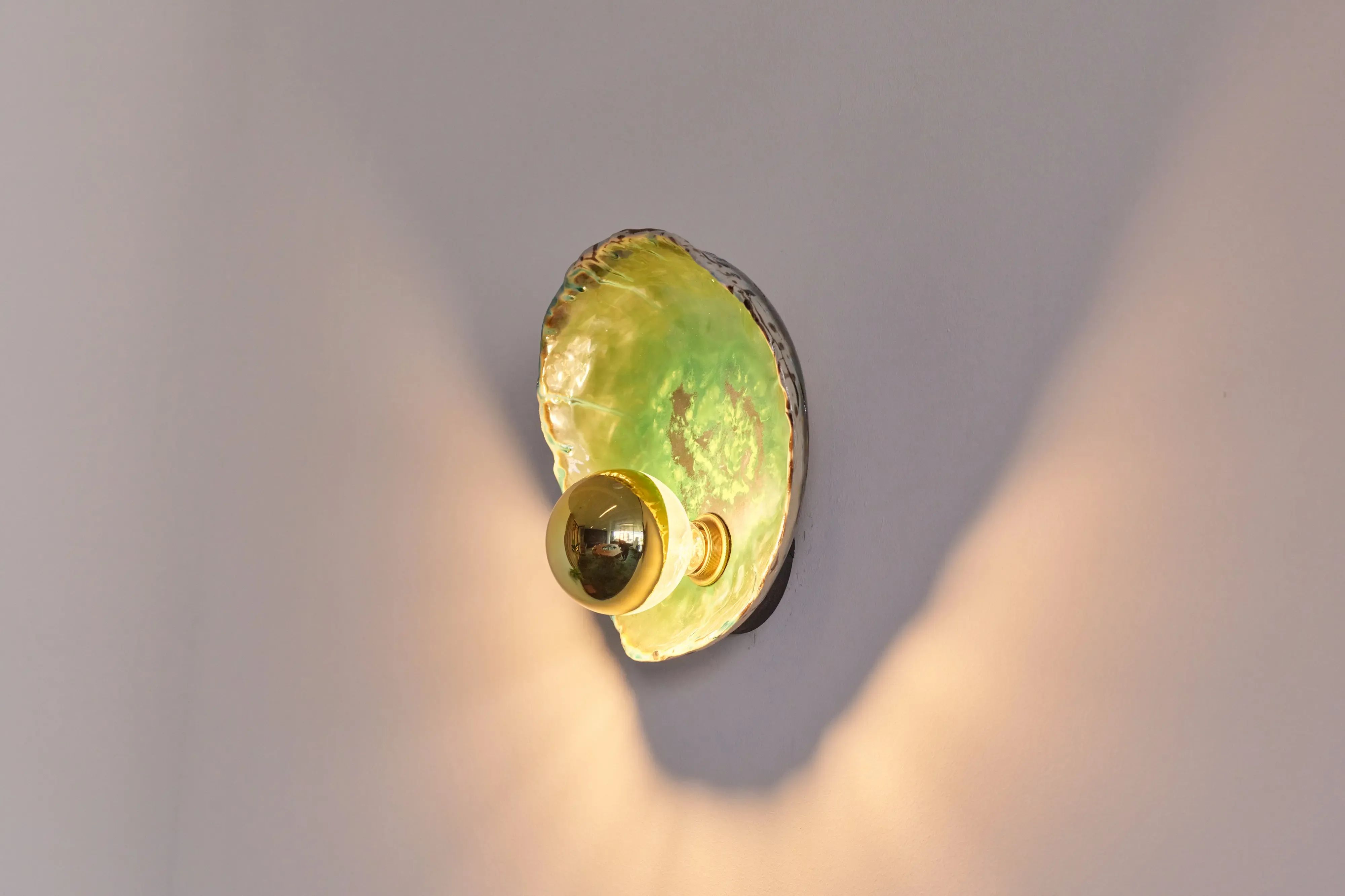 Kleurrijke groene wandlamp van een schelp die warm licht verspreidt.