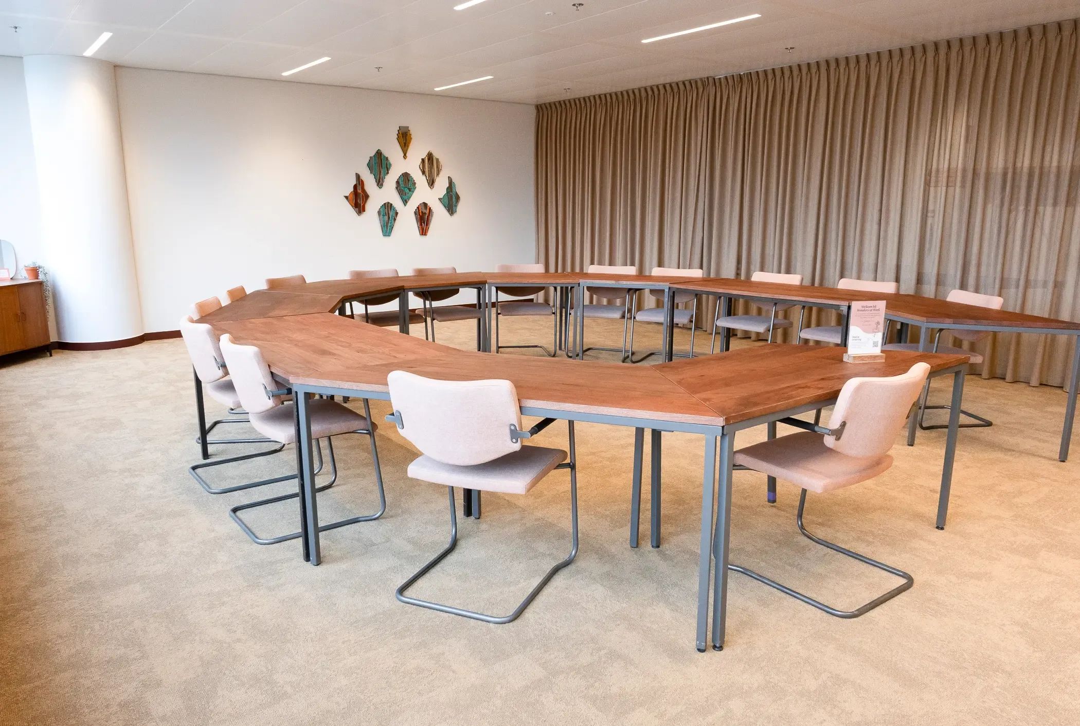 Moderne vergaderruimte met een U-vormige houten tafel, lichte stoelen en decoratieve wanddecoratie.