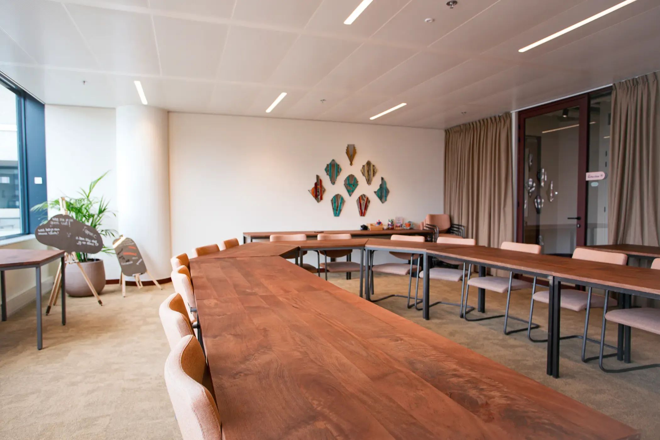 Moderne vergaderruimte met een grote, gebogen houten tafel met stoelen en natuurlijk licht door een raam.