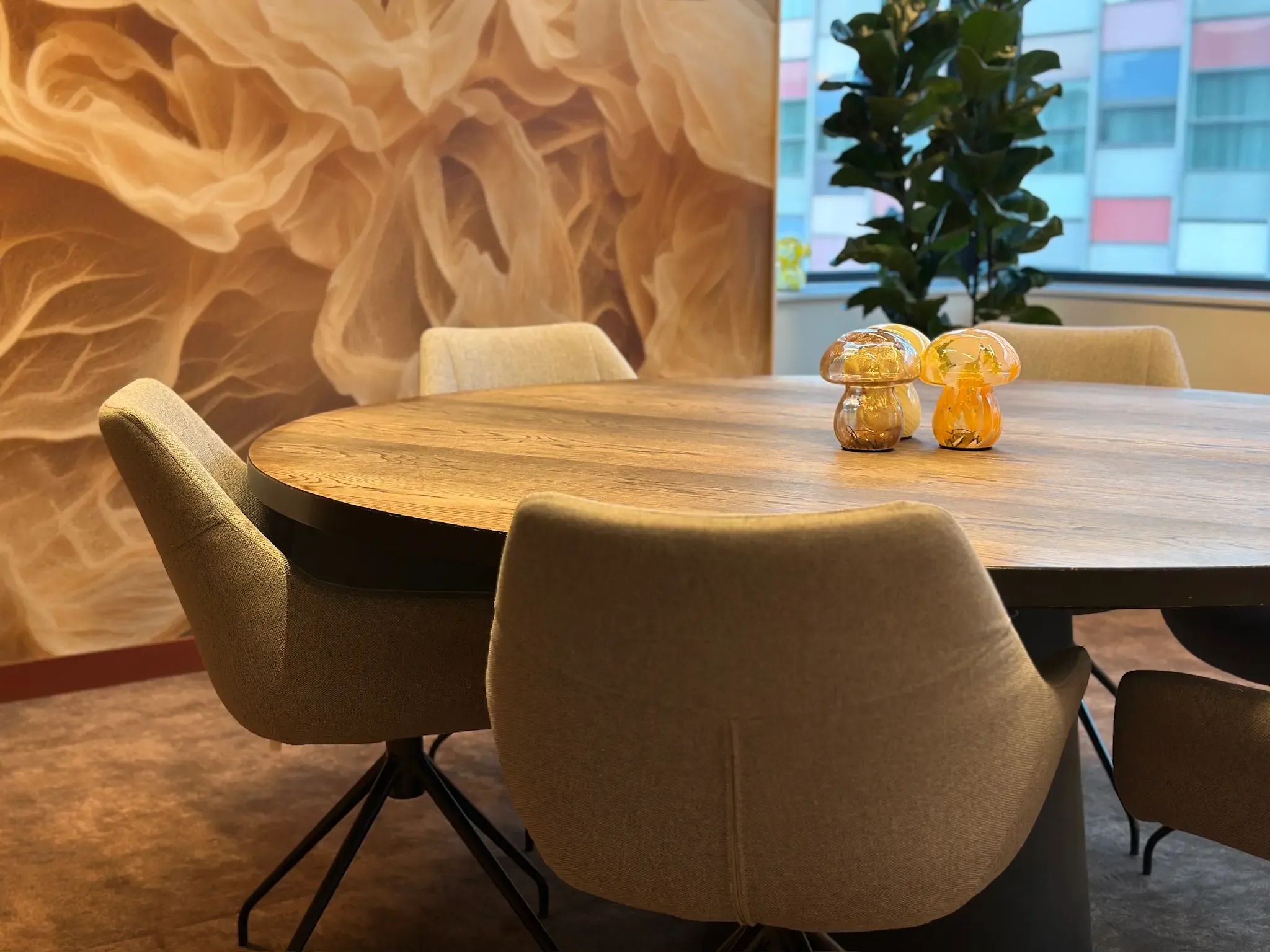 Moderne vergaderruimte met een ronde houten tafel, lichte stoelen en een muur met abstract patroon.