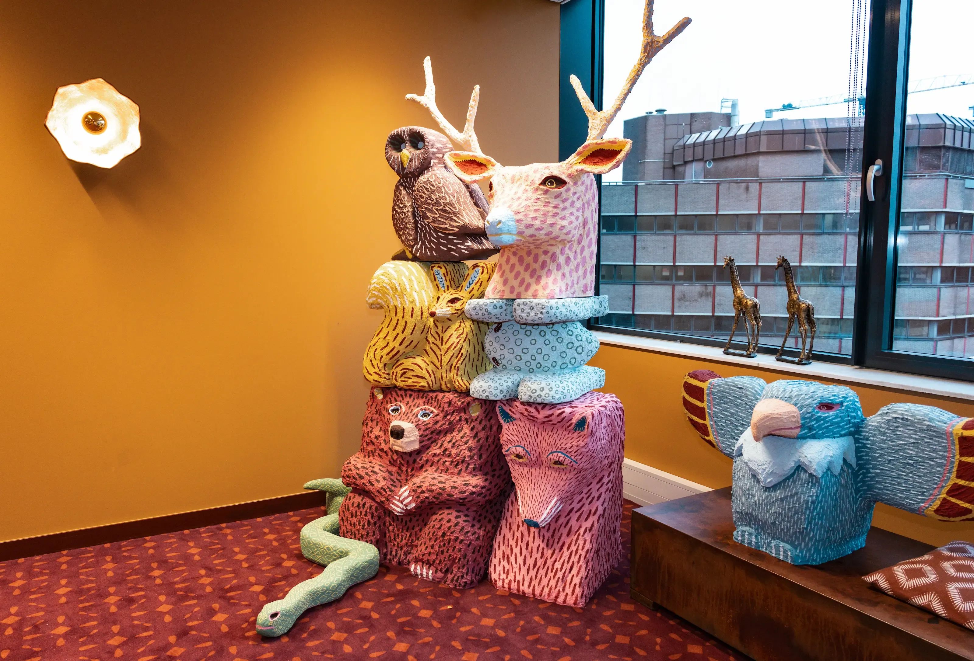 Gestapelde kleurrijke gebreide dierensculpturen, waaronder een beer, uil en hert, in een modern interieur.