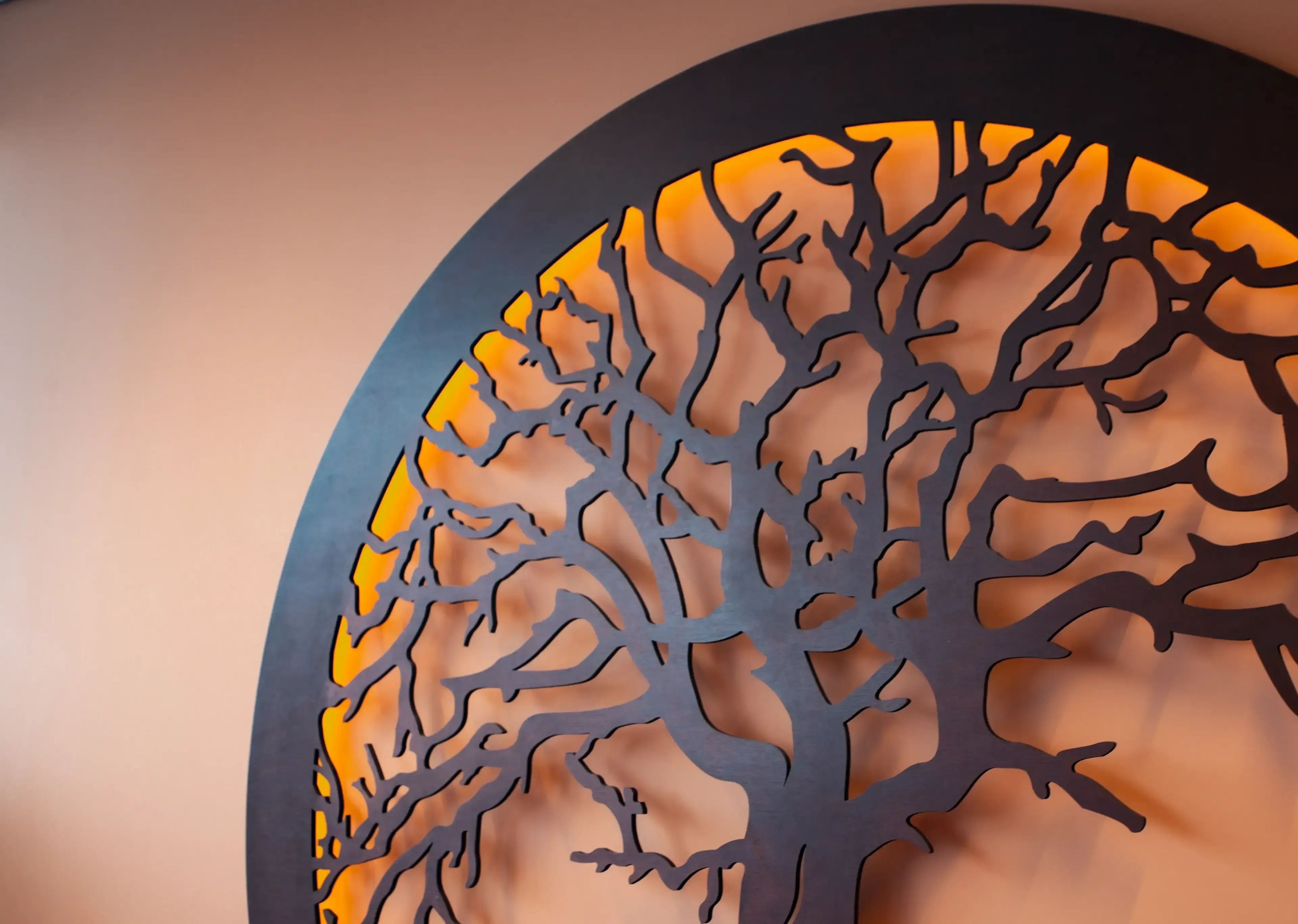 Close-up van een decoratief zwart metalen boomsilhouet met warme oranje achtergrondverlichting.