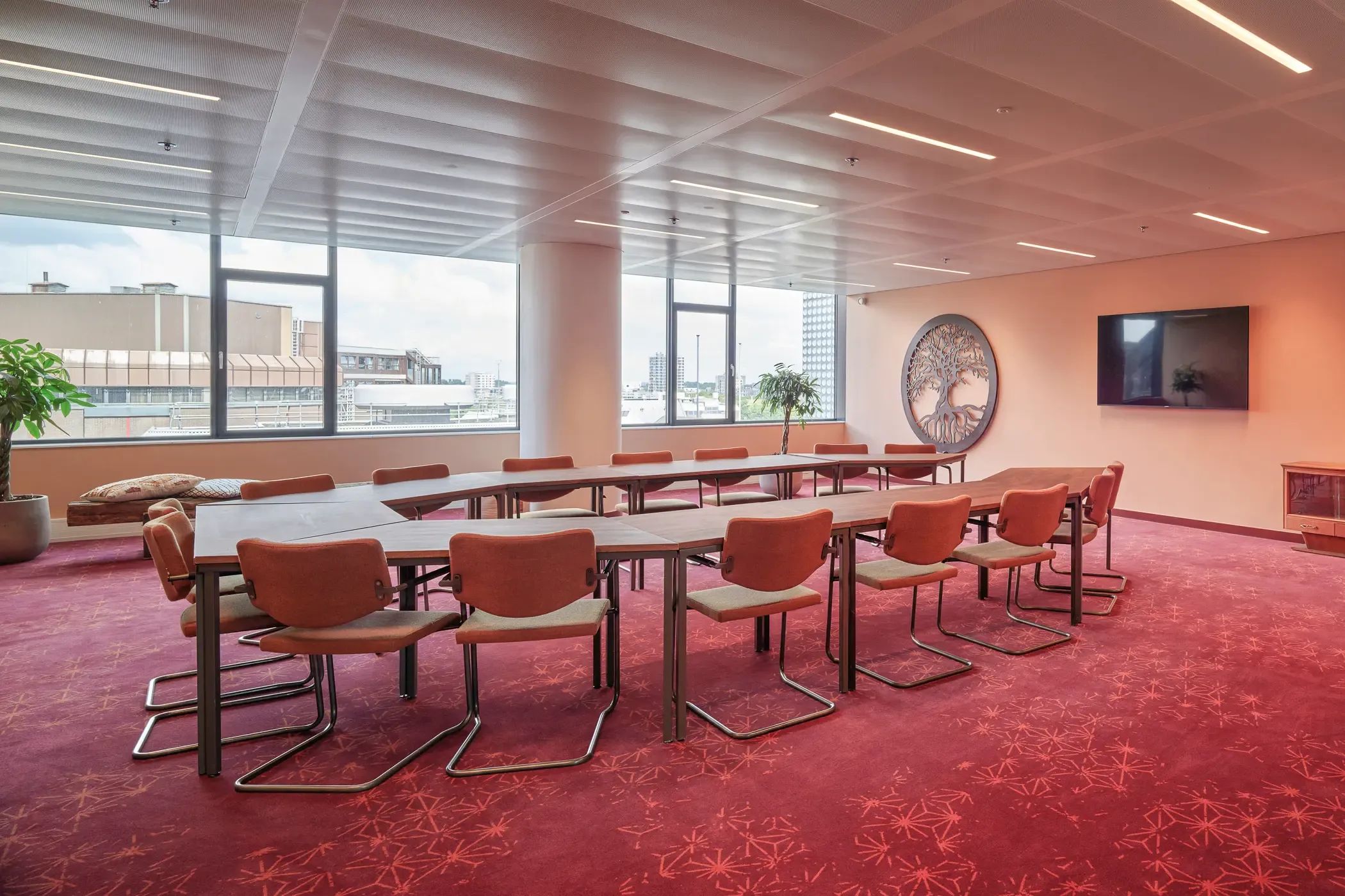 Ruime, moderne vergaderzaal met een lange tafel, bruine stoelen en grote ramen.