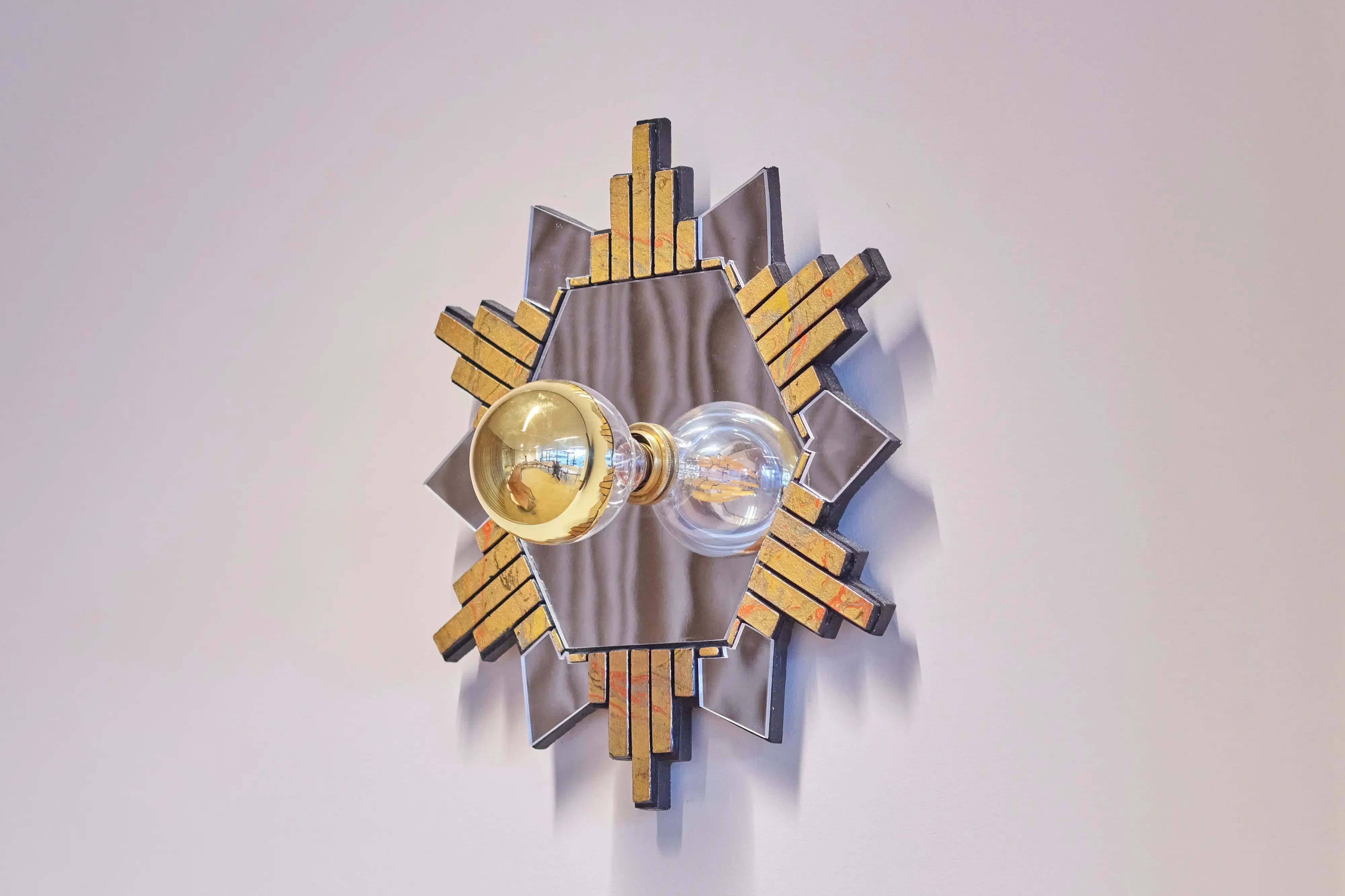 Geometrische wandlamp met gouden en grijze accenten en twee opvallende lampen.
