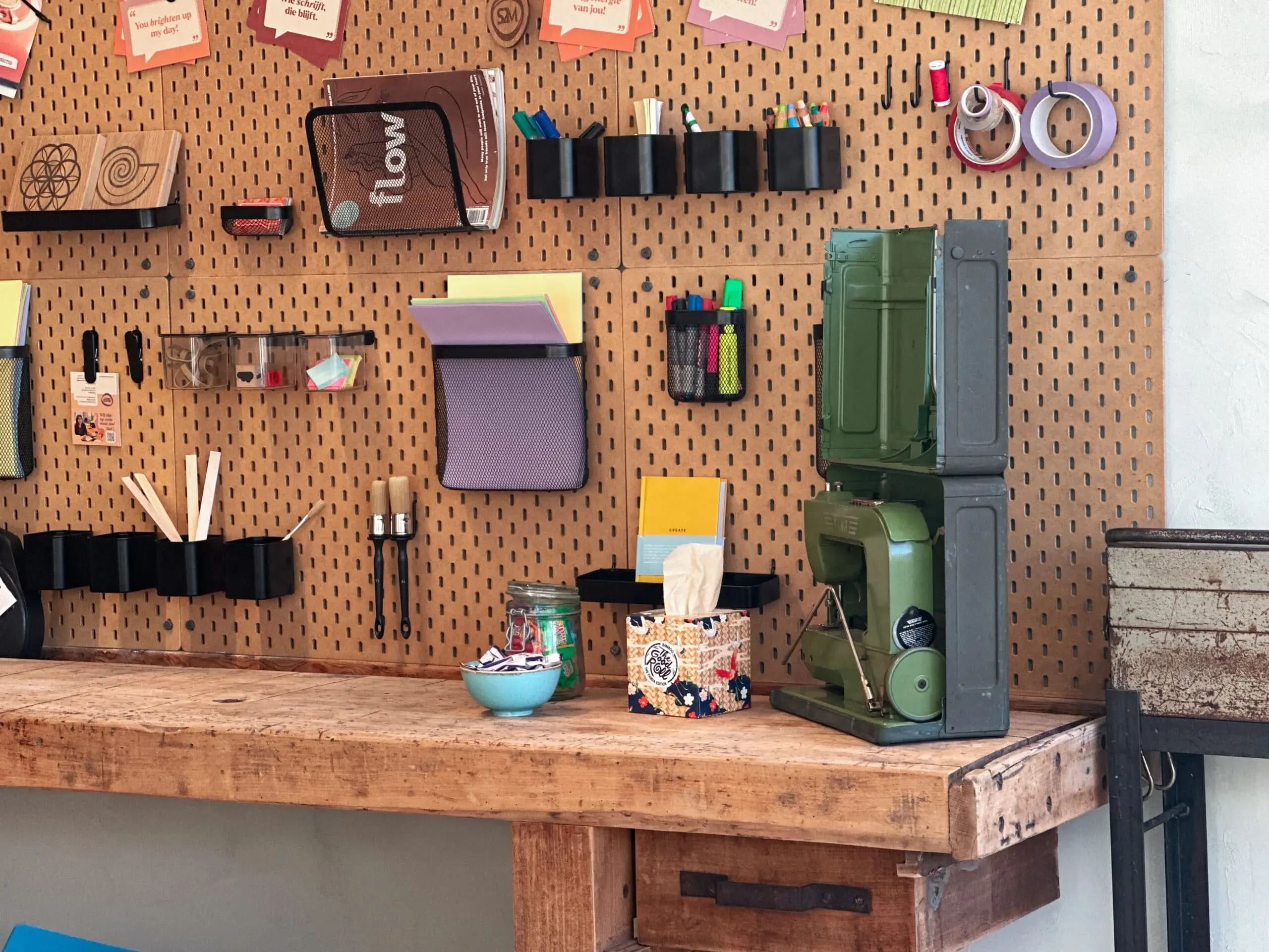 Een werkbank met allemaal creatieve spullen erop. De werkbank staat in een middelgrote vergaderruimte