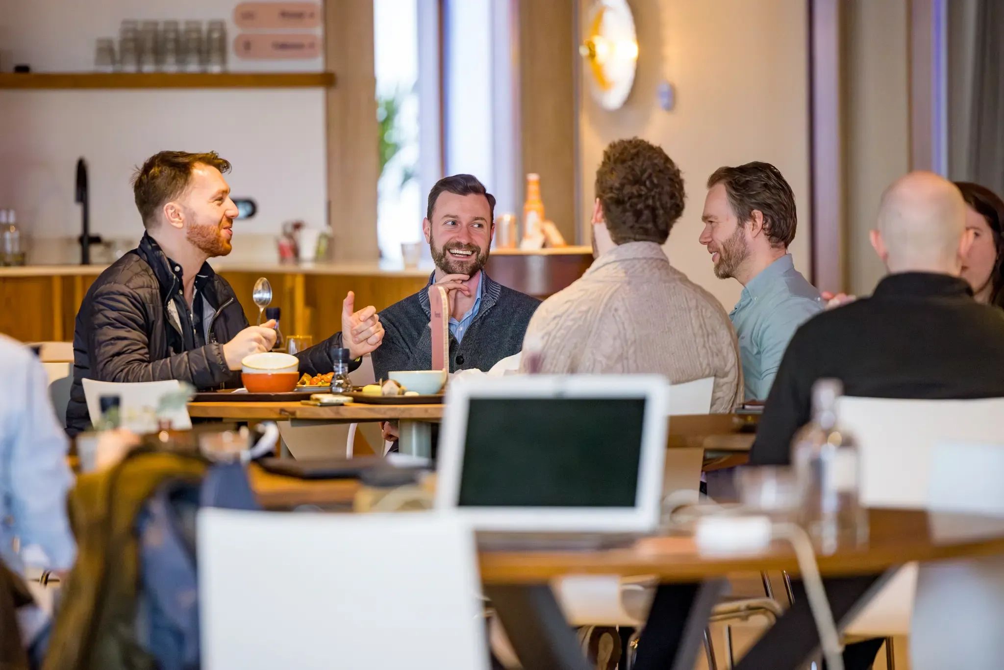 Group of men conversing cheerfully at a cafe table with drinks and food.