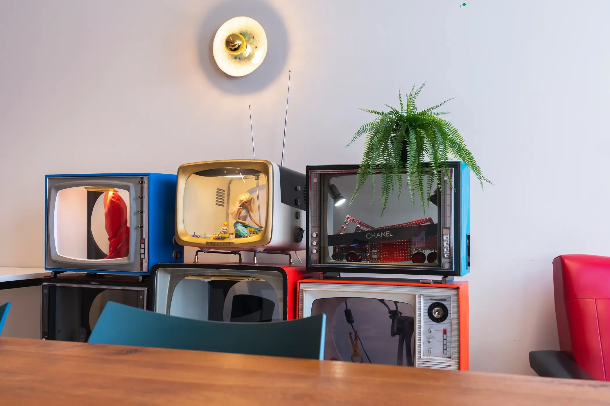 Gestapelde vintage televisies met antennes en een plant op een witte muur.